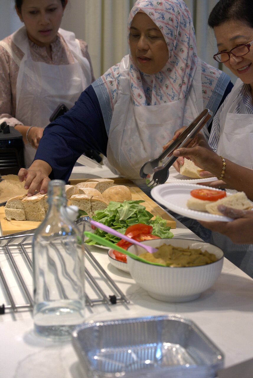 Participants spreading Beverly's eggplant dip onto fresh ciabatta with tongs, plated with tomato and lettuce