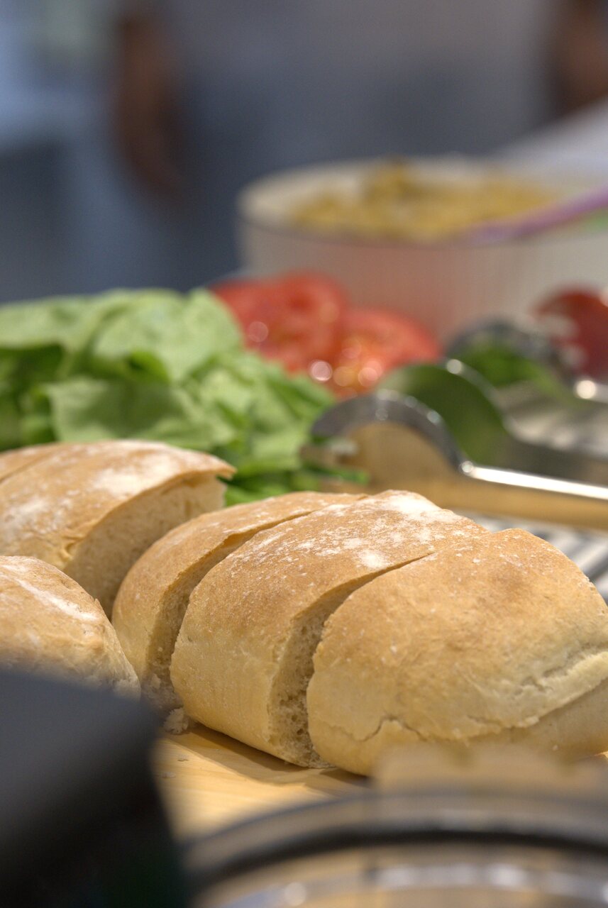 Close-up of sliced ciabatta bread with lettuce, tomato and eggplant dip in the background