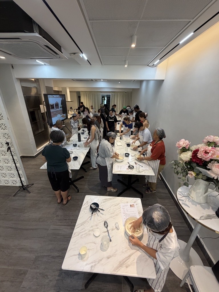 A young baker mixing focaccia dough in the foreground with the full workshop behind